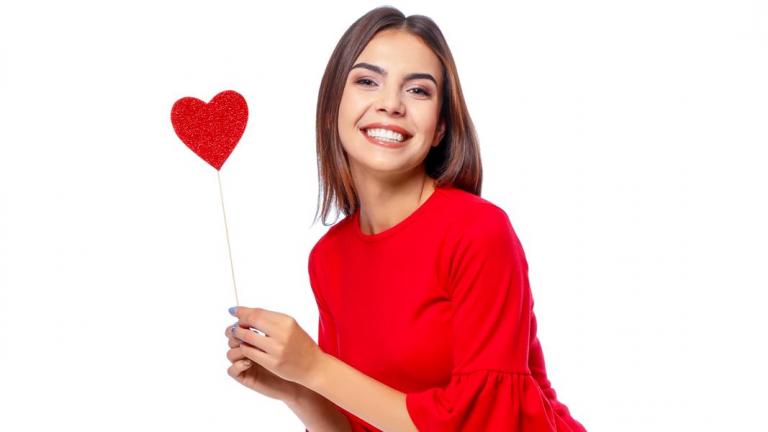 Woman wearing red on a white background, holding a red heart-shaped sign.