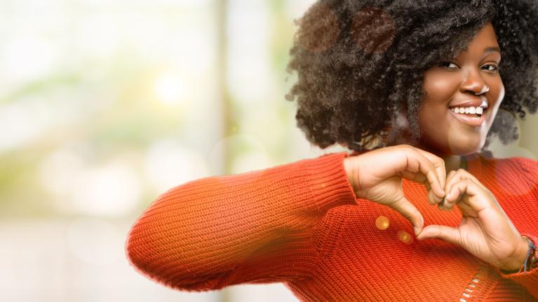 A woman is smiling and making a heart shape with her hands.