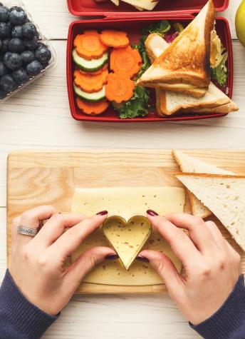 An image of someone making a heart shaped cheese slice for their lunch.